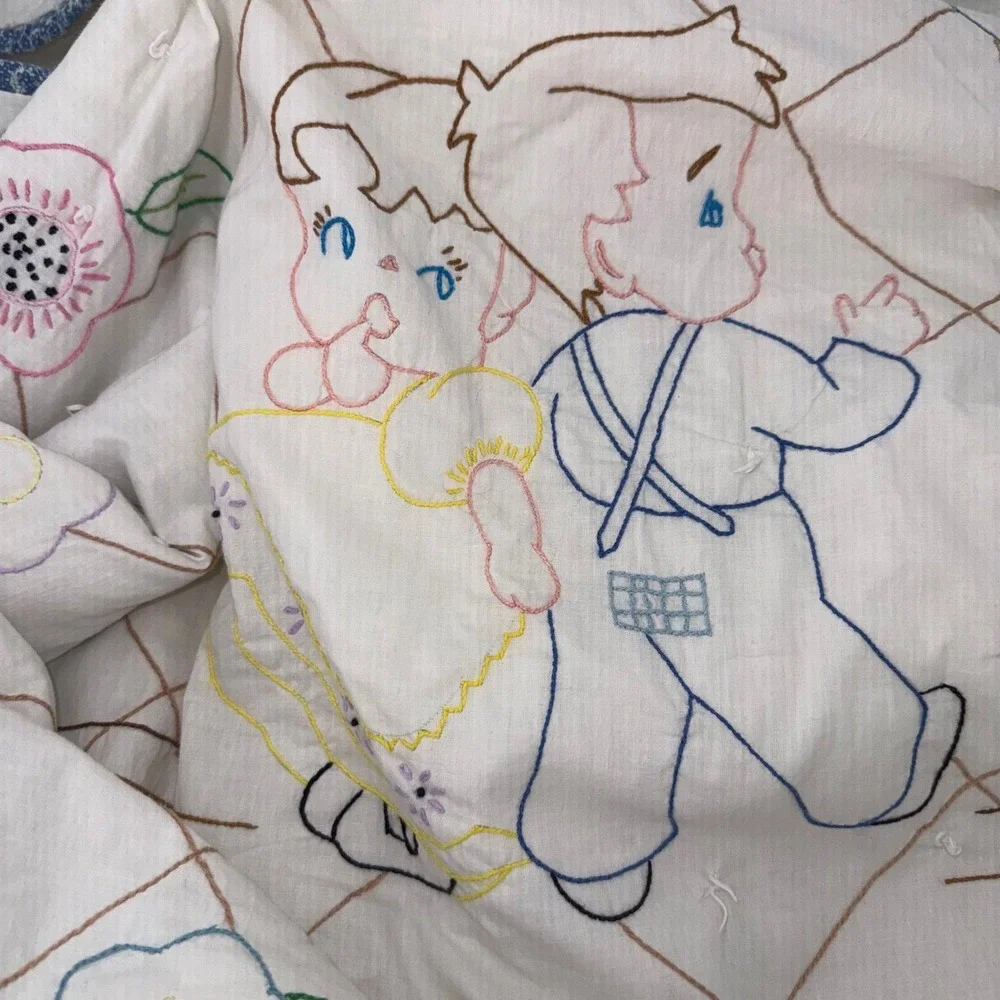 Vintage baby quilt featuring embroidered figures and floral motifs 35.75